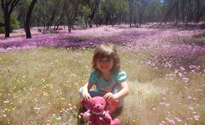 Grace Fulton sits with a stuffed toy in a field of colourful flowers 